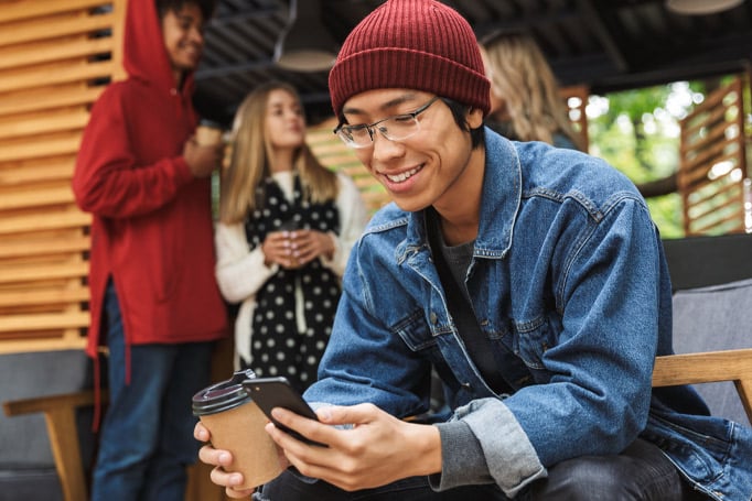 Man sitting outside coffee shop holding a cup of coffee and looking at his phone