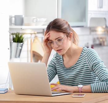 A woman using a laptop at a kitchen table with a smartphone nearby.